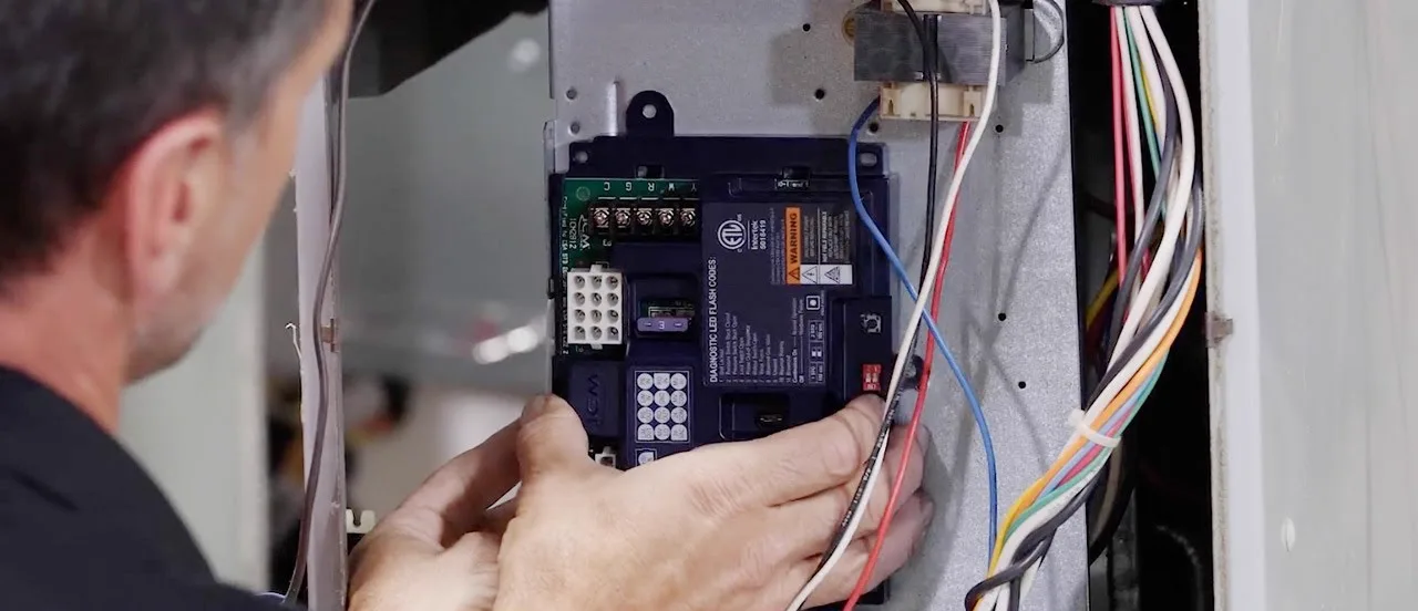Technician fitting an ICM2812 universal furnace control board into a furnace cabinet