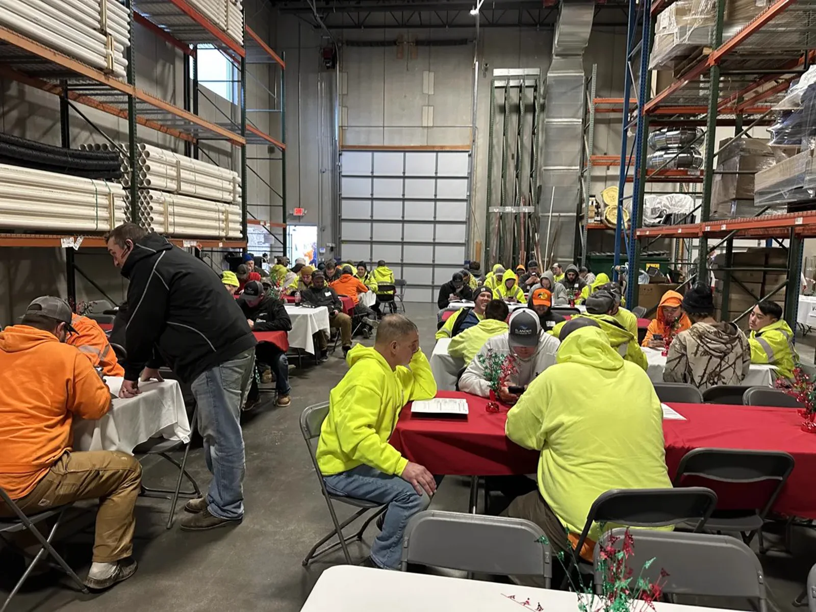 Contractors in high-visibility sweatshirts seated at tables for a session held inside a warehouse